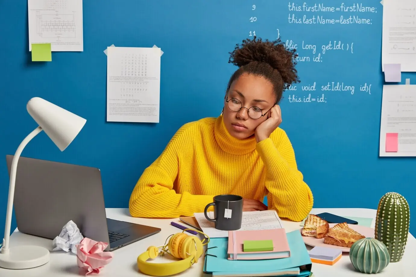 Eine ernste, konzentrierte Studentin nutzt einen Online-Bildungsdienst, sieht sich auf dem Laptop ein Trainingswebinar oder einen Kurs an, hat viele Dinge auf dem Tisch und trinkt Tee.